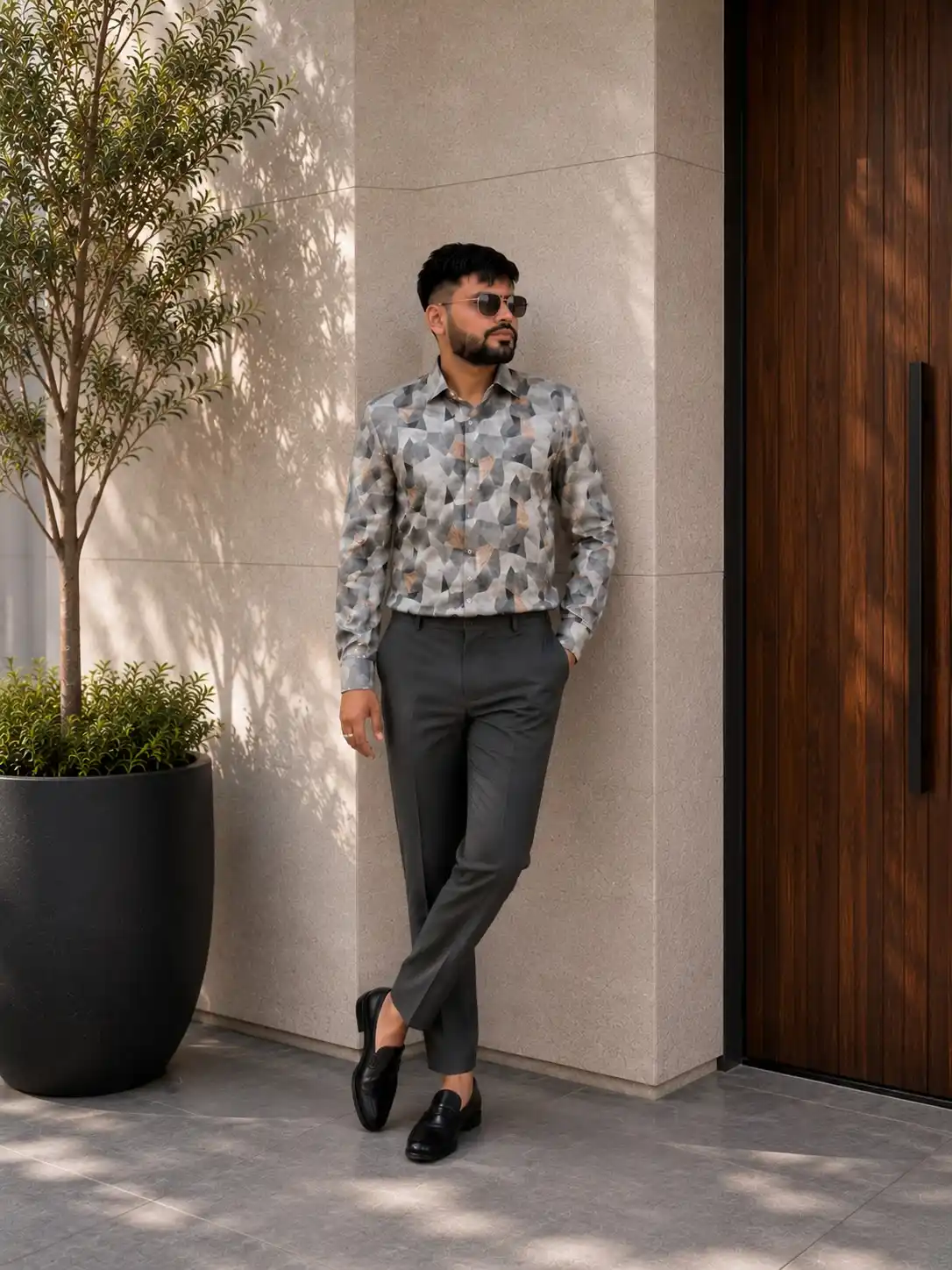 17 Resort‑Ready Men’s Outfits for Tropical Vacations 16 15. Geometric Patterned Shirt and Charcoal Trousers
A grey long sleeve button down shirt featuring a bold geometric print brings an artistic edge to vacation fashion. This eye catching top in men’s resort print shirt look.webp contrasts sharply with tailored charcoal trousers. Tucking the shirt into slim fit pants maintains a highly polished appearance.Black leather loafers offer a sophisticated finishing touch for evening wear. Dark round sunglasses complement the sharp lines of the outfit. You can choose this refined ensemble for upscale resort dinners or cocktail lounges.