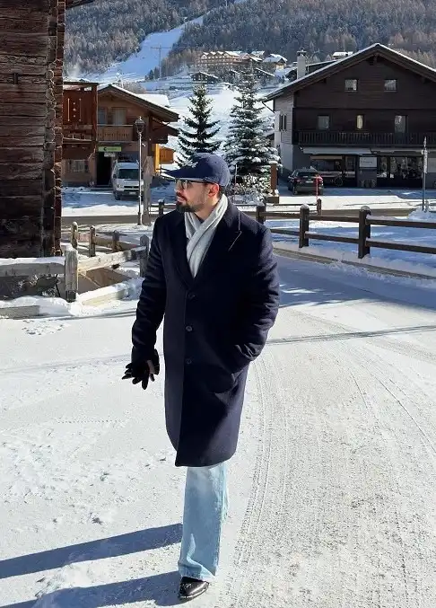 25 Stylish Winter Travel Outfits for Men & Ski Trips 13 Navy Overcoat With Light Wash Jeans for Walking Through Town